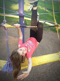 Portrait of playful girl hanging on outdoor play equipment at ground