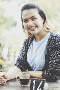 Portrait of smiling young woman with coffee on table