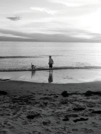 Rear view of boy with dog at beach against sky