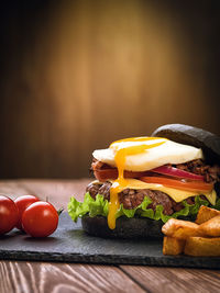 Black burger with an egg on a stone plate. cherry tomatoes. fried potatoes.