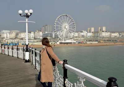 Woman standing on pier at brighton beach against sky