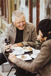 Smiling senior man sharing smart phone with woman in cafe