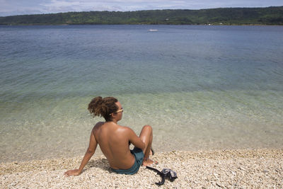 Rear view of shirtless man sitting on beach