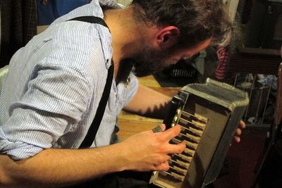 Side view of young man playing accordion at home
