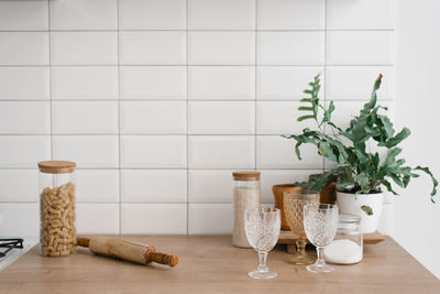 A glass jar with pasta, glasses, a rolling pin and a houseplant stand in the bright kitchen