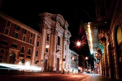 People walking on illuminated street amidst buildings in city at night