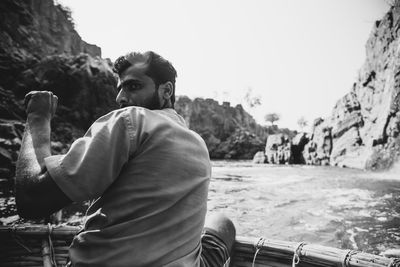 Man sitting on rock against sky