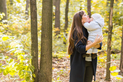 Mother and daughter standing against trees