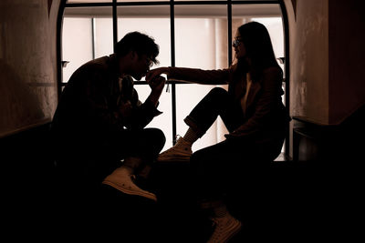 Side view of man kissing woman hand while sitting on window sill at home