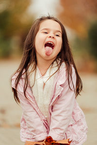 Cute girl holding autumn leaf while making face outdoors