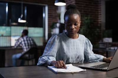 Young woman using laptop while talking on phone at office graph