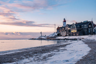 Lighthouse by sea against sky during sunset