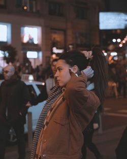 Close-up of woman tying hair in city at night