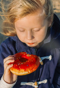 Girl in delight eats donut with red icing, food stained her mouth