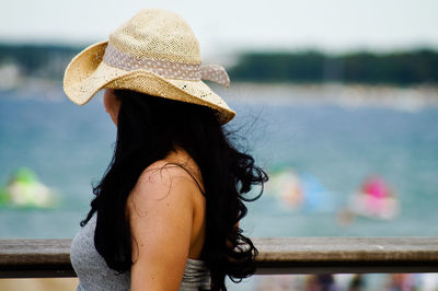 Side view of woman wearing sun hat standing at railing against sea