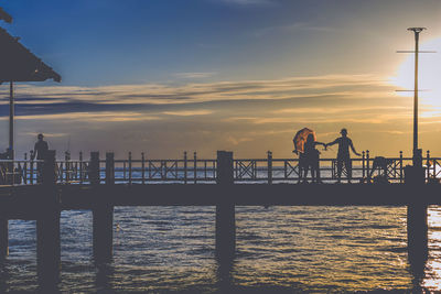 Silhouette people standing on pier by sea against sky during sunset