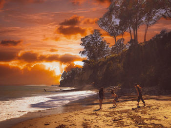 People on beach against sky during sunset