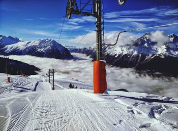 Ski lift poles on snow covered landscape by mountains against sky