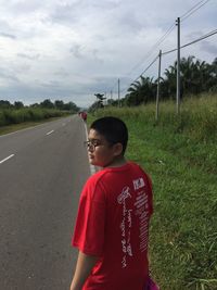 Rear view of boy walking on roadside against sky