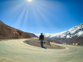Rear view of man walking on mountain road against blue sky
