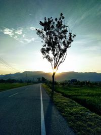 Empty road amidst field against sky during sunset