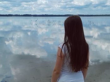 Rear view of woman standing at beach against sky