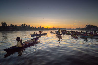 People in boats on river against sky during sunset