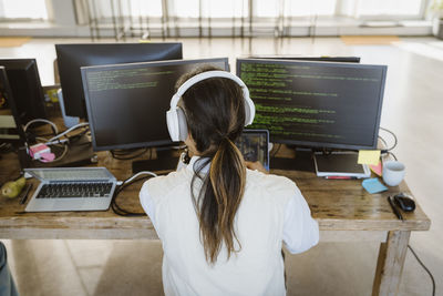 Rear view of male programmer working on computer at desk in creative office