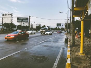 Cars on wet street in city against sky