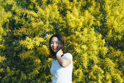 Portrait of young woman standing against yellow flowering tree