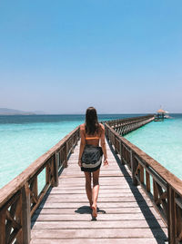 Rear view of man walking on pier by sea against clear sky