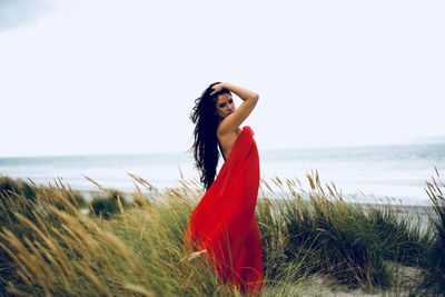 Portrait of young woman posing at beach in sea against sky