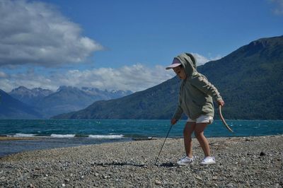 Cute girl playing at lakeshore by mountains against blue sky