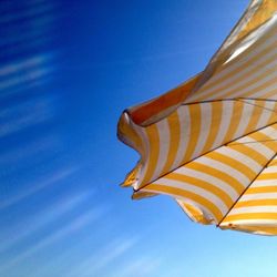 Low angle view of striped parasol against clear blue sky