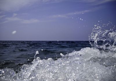 Sea waves splashing on shore against sky