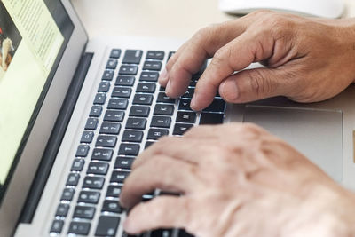 Cropped hands of man typing on laptop keyboard