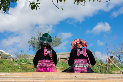 Rear view of women wearing traditional clothing while sitting against cloudy sky