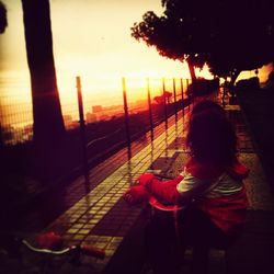 Side view of woman standing by railing against sky during sunset