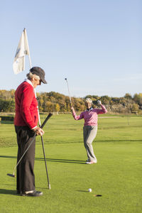 Senior woman celebrating golf shot while friend holding flag on course