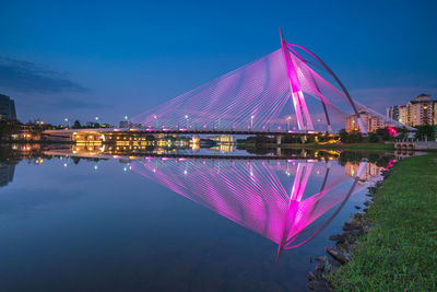 Illuminated city by river against sky at night