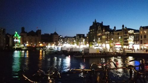 River by illuminated city against clear sky at night