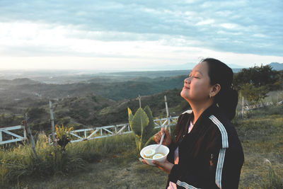 Side view of young woman looking at view of sea against sky