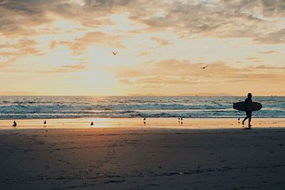 Silhouette man standing on beach against sky during sunset