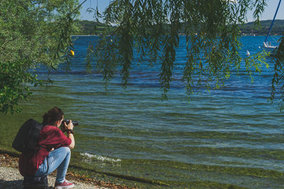 Rear view of man photographing woman standing by lake