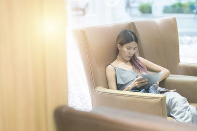 Young woman using smart phone while sitting on laptop