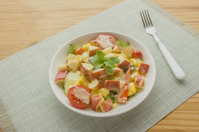 Mixed vegetable and fruit salad with crab sticks on a white plate, ready to serve