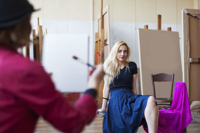 Artist holding paintbrush against woman sitting on table