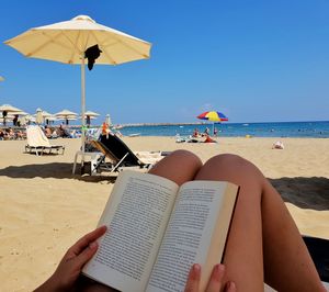 Midsection of woman with book relaxing at beach