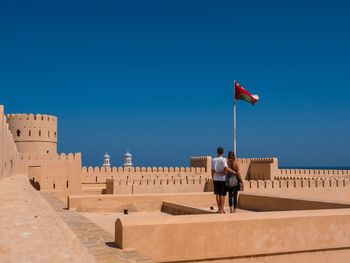 Rear view of man and woman walking against clear blue sky