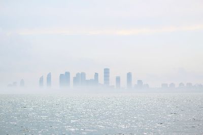 Modern cityscape by sea against sky during sunset